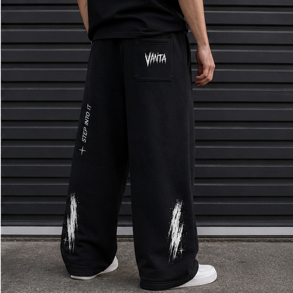Vanta unisex black fleece sweatpants with white graffiti-style logo and Step Into It text on a relaxed oversized fit.